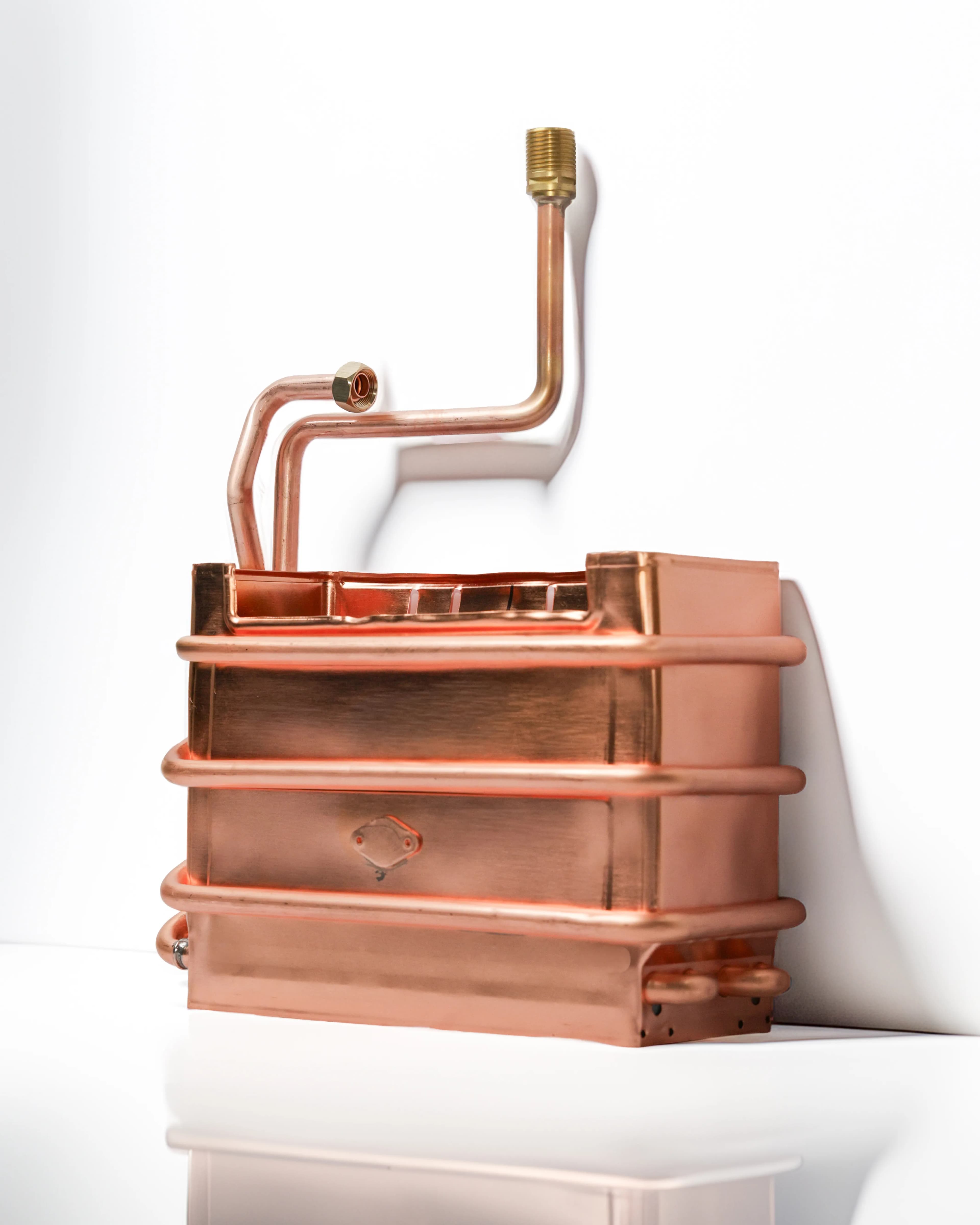 Copper heat exchanger with brass fittings, photographed on white