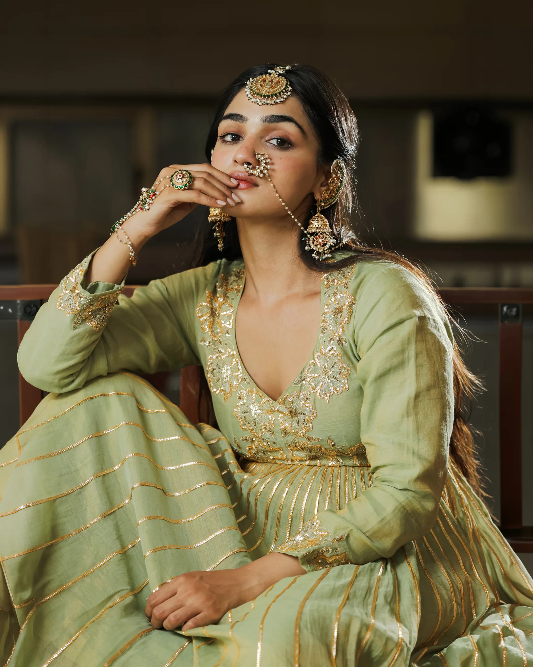 Close portrait of the model in statement jewellery and a green embroidered anarkali, hand raised to her face