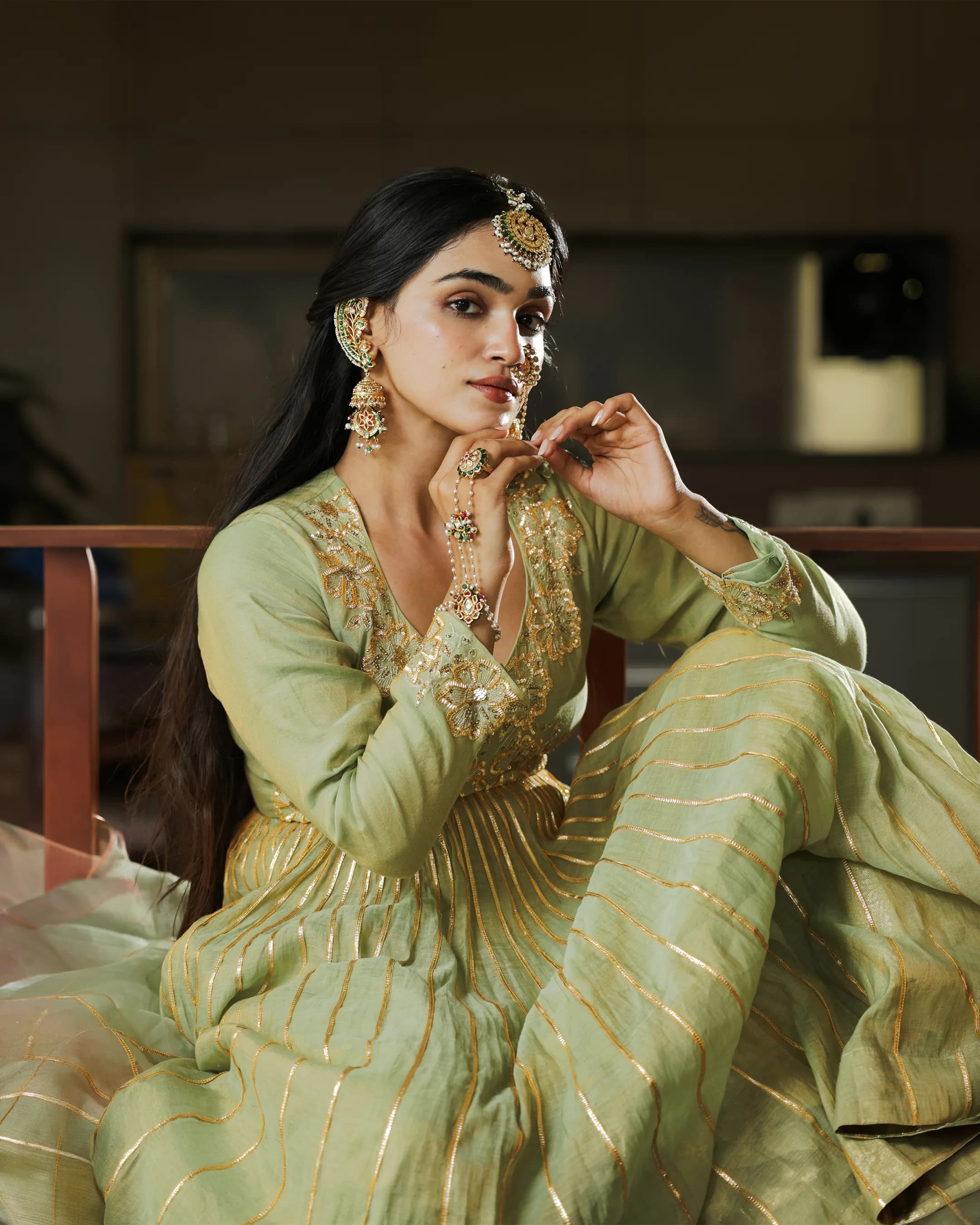 Model in a green anarkali with sequin florals and a pearl hand harness, seated and looking over her shoulder