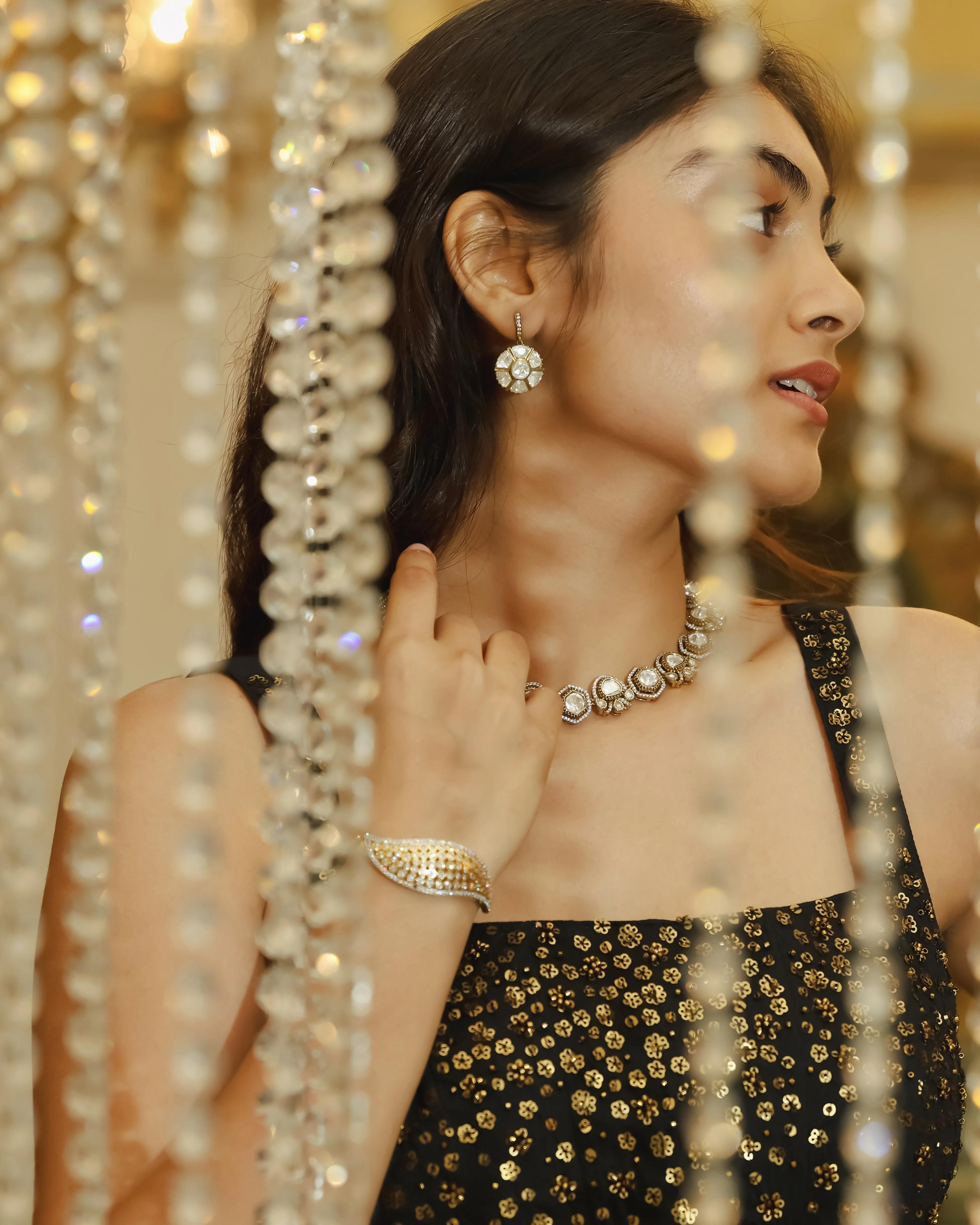 Model in a black sequinned top wearing a statement choker, earrings and cuff, framed by hanging crystal strands