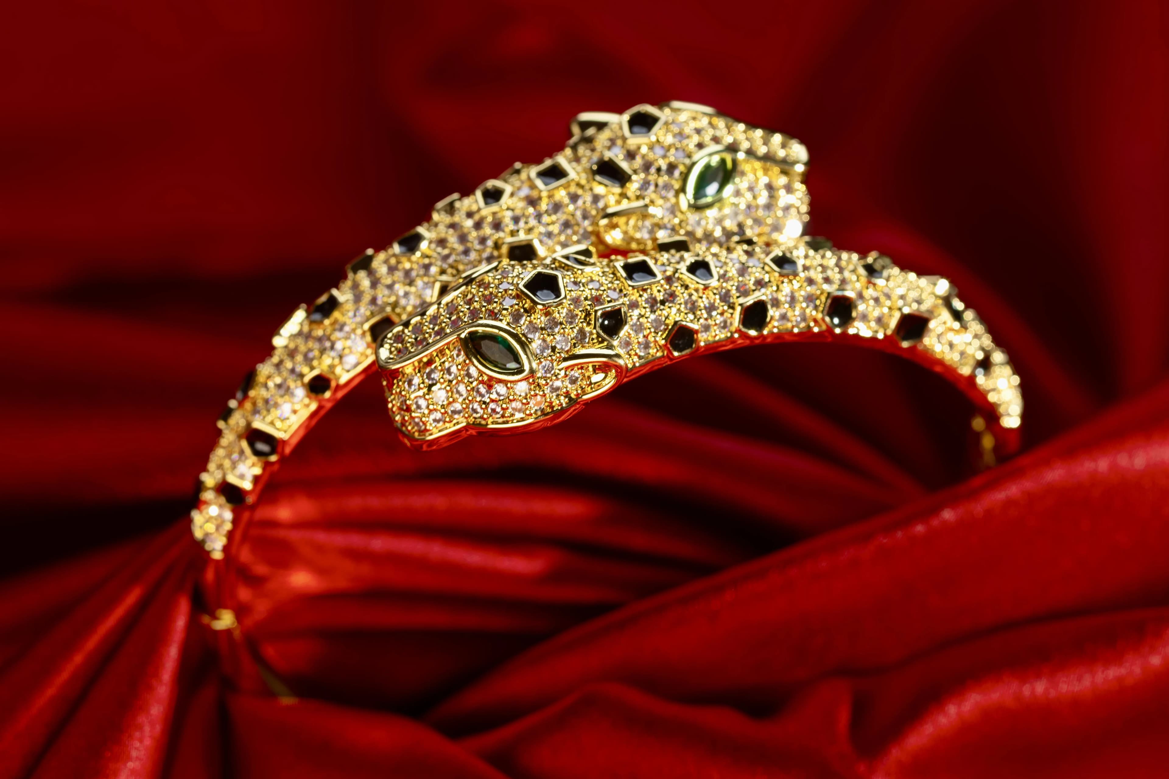 Gold double-headed panther bangle with pave stones, black enamel spots and green eyes on red satin
