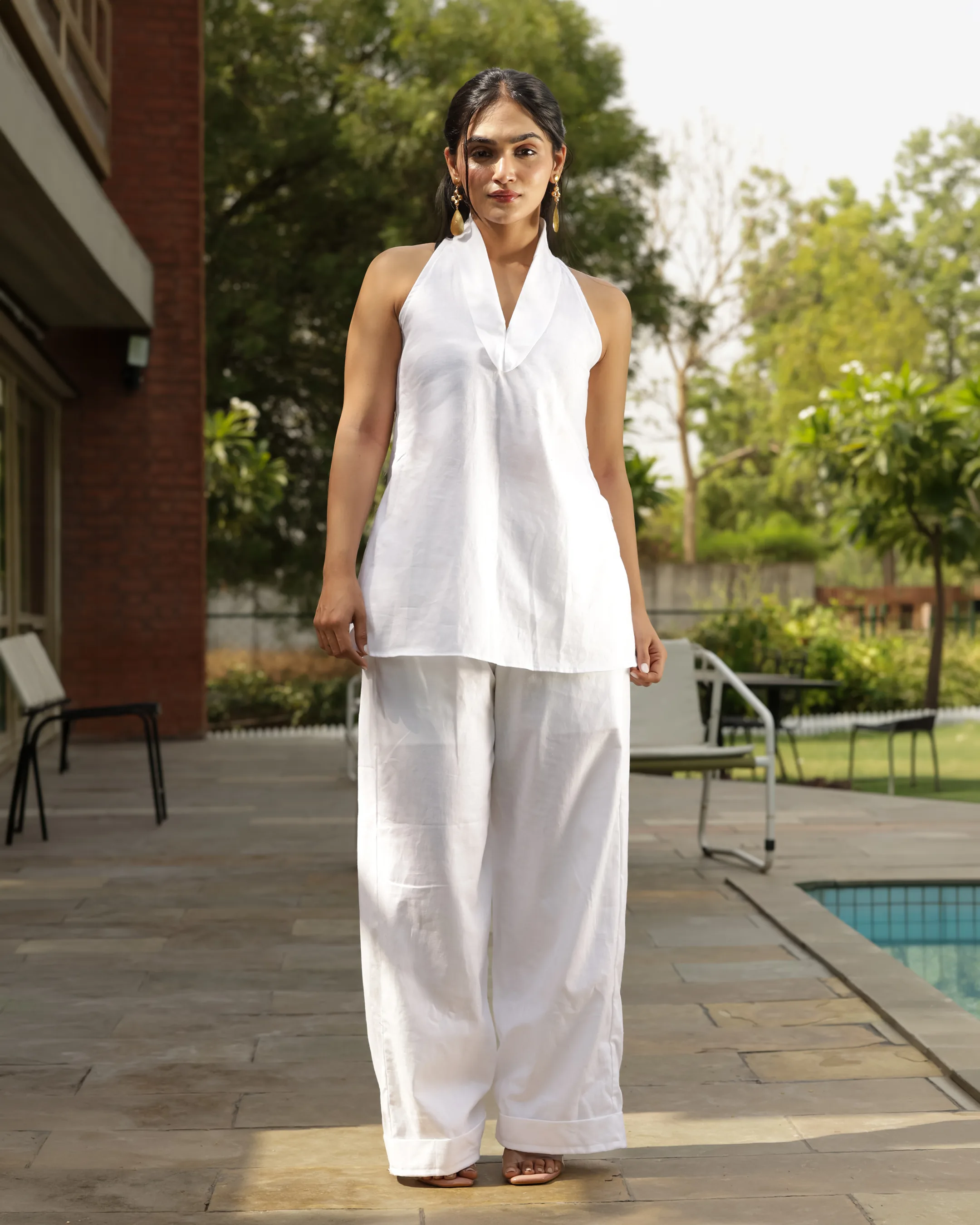 Model in a white halter top and wide-leg trousers standing by a pool