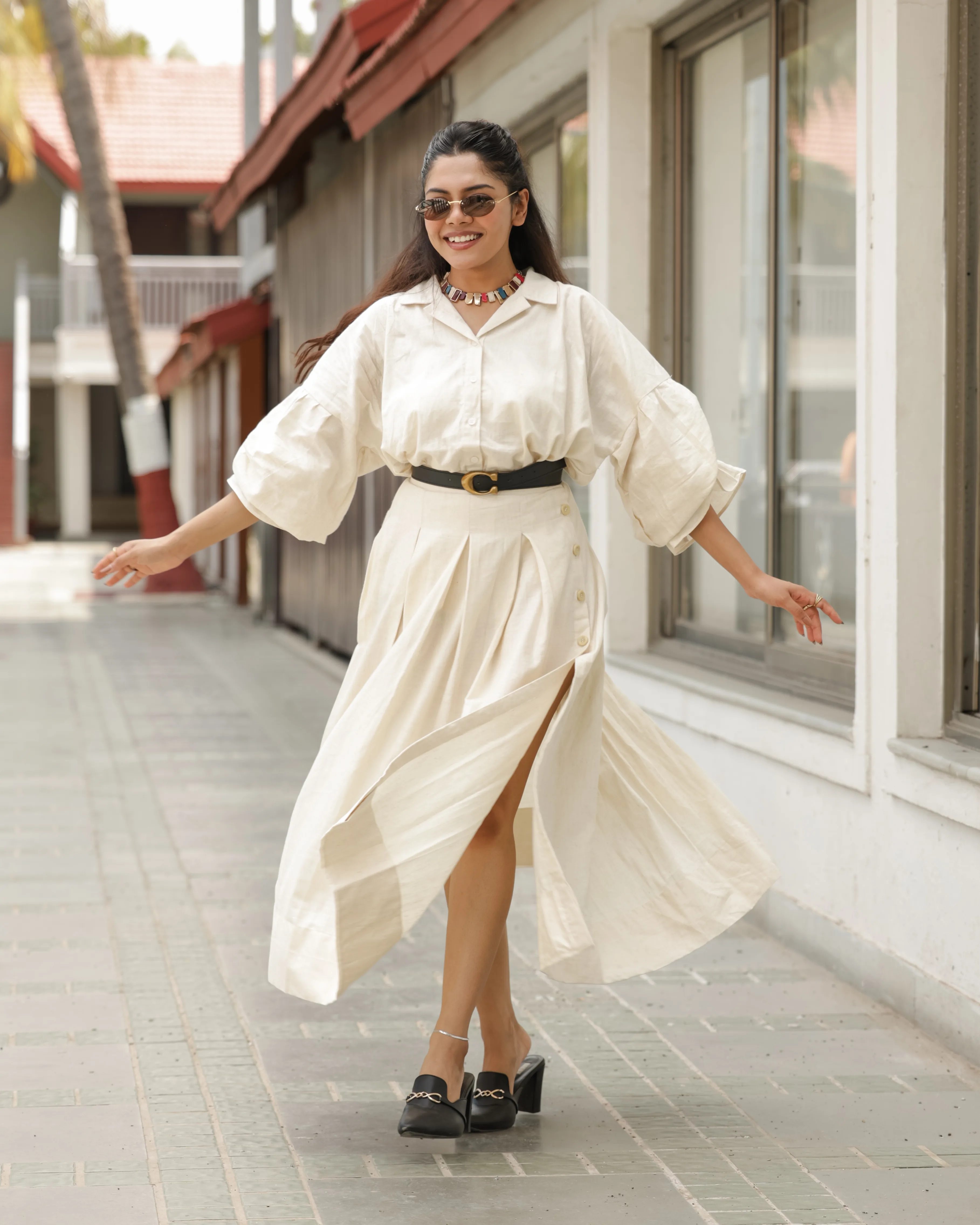 Smiling model twirling in a cream shirt and pleated button skirt with a black belt