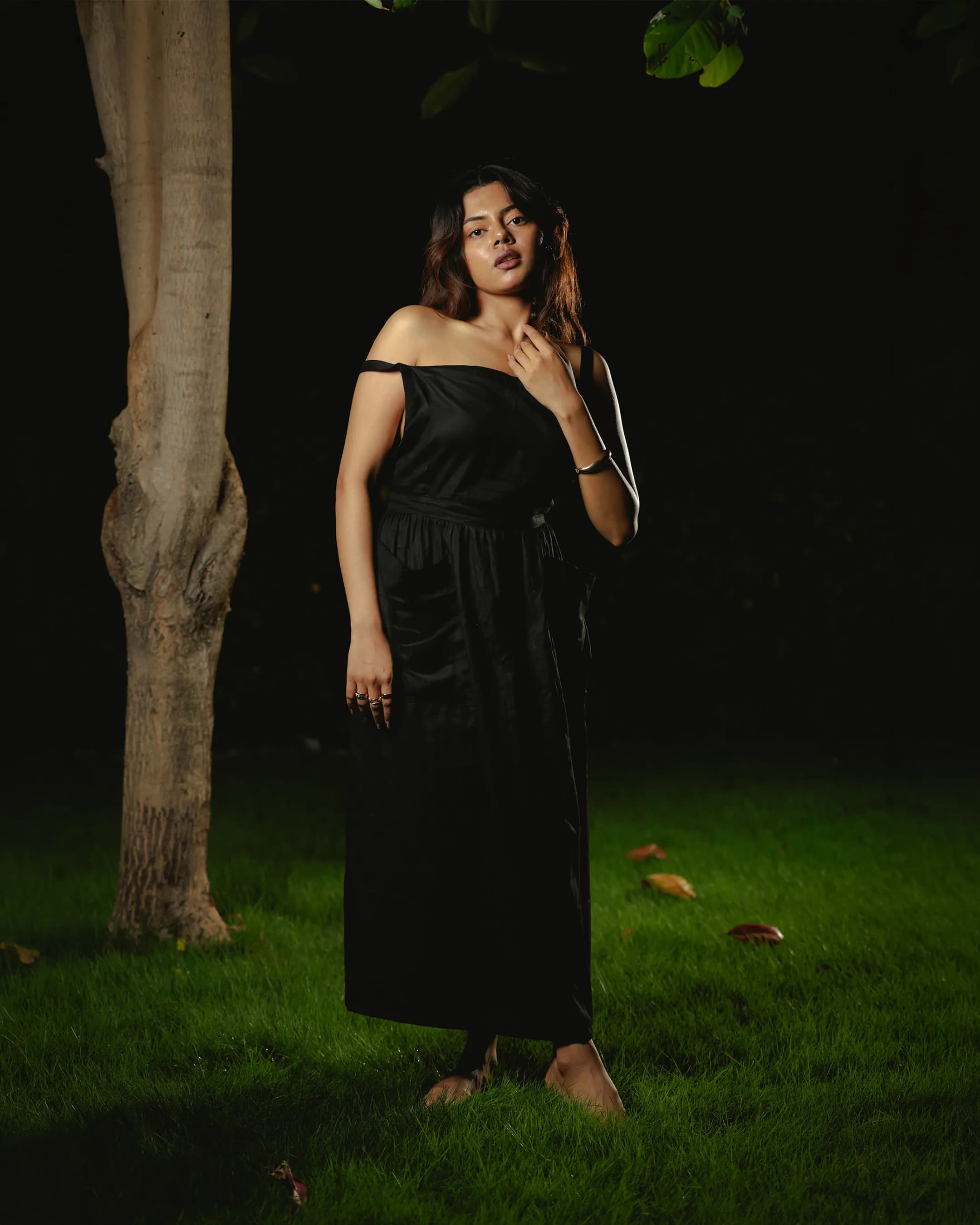 Model in a black one-shoulder midi dress lit at night on a lawn