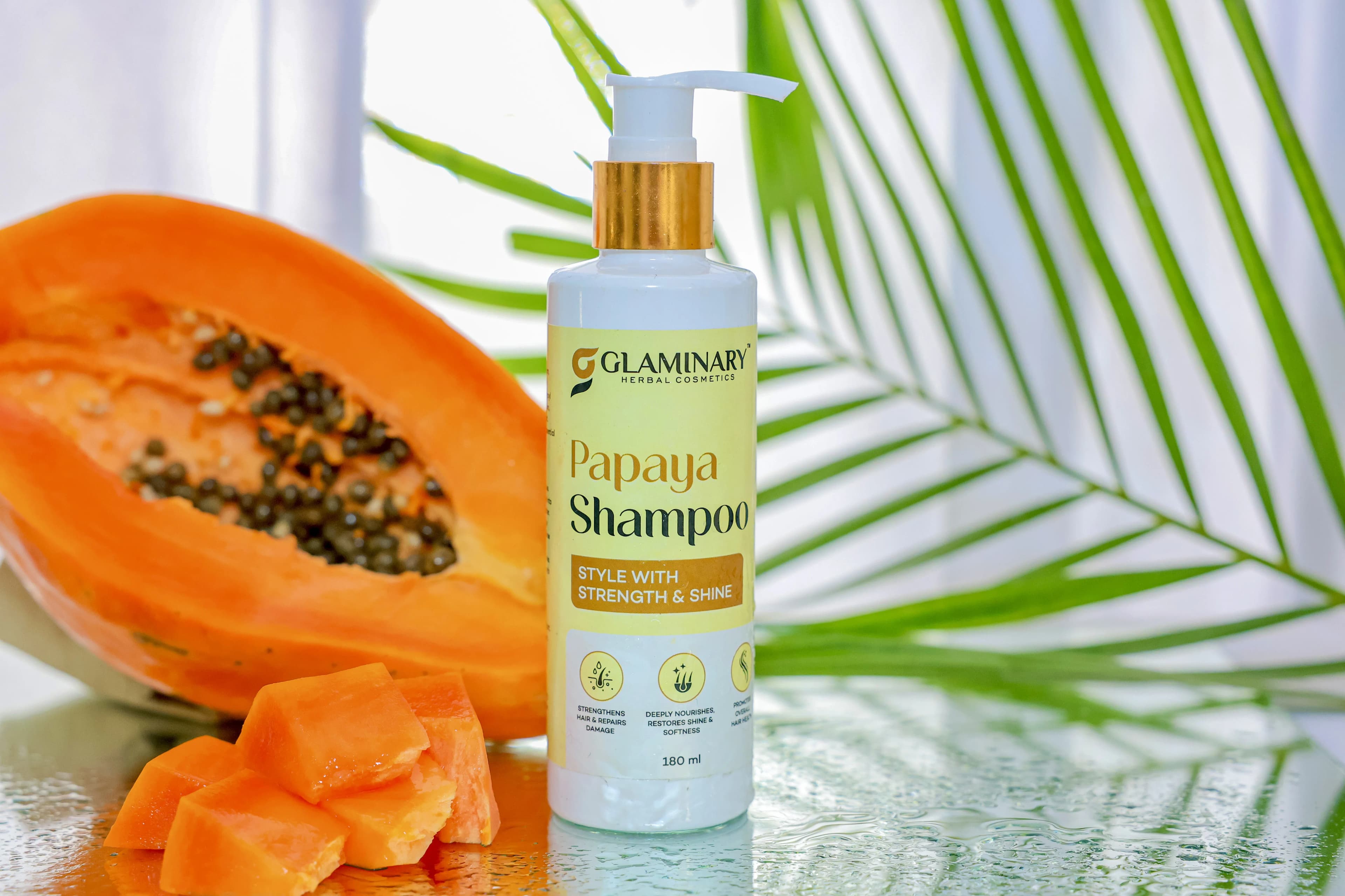Glaminary Papaya Shampoo bottle beside a halved papaya and a palm leaf