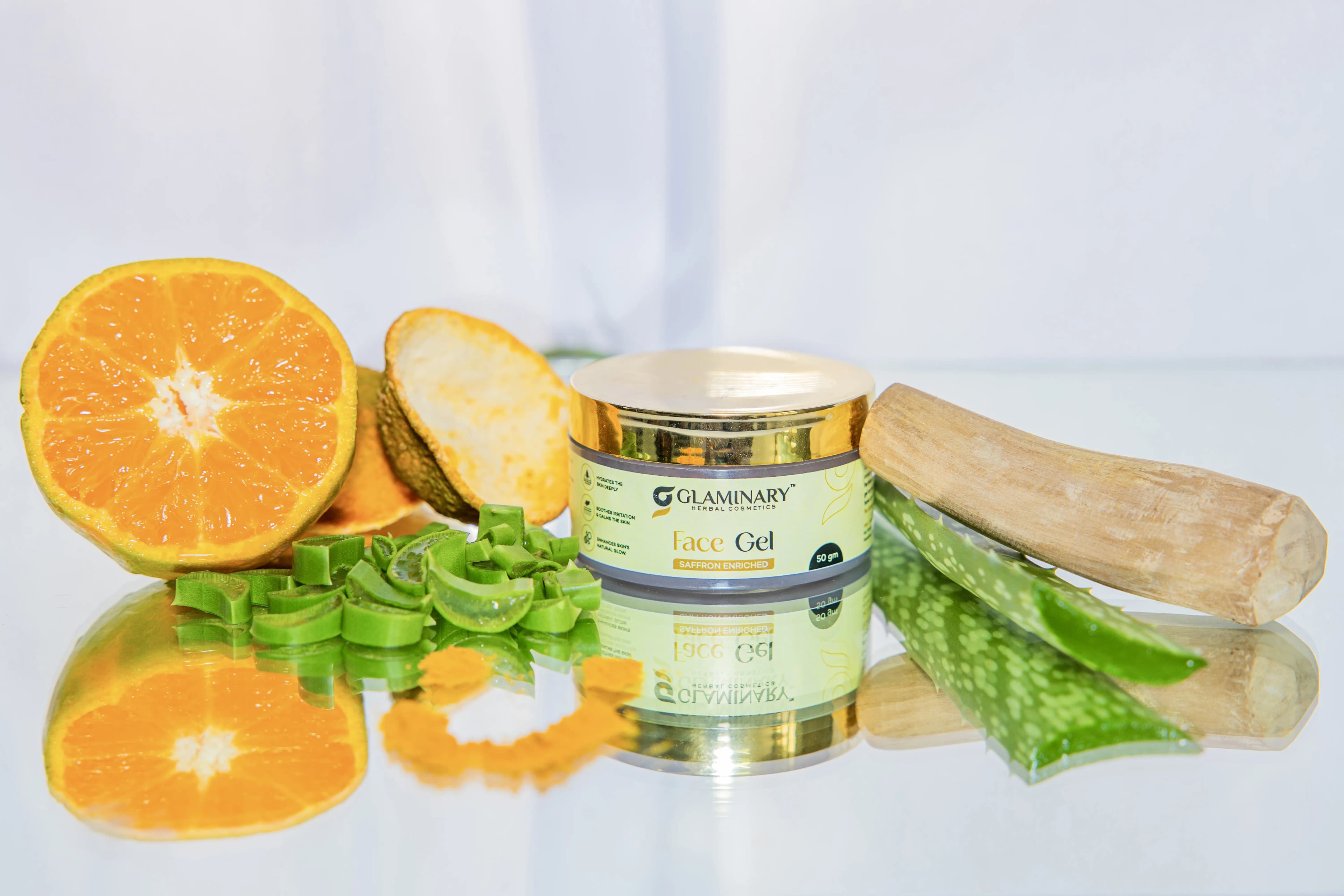 Glaminary Face Gel jar with a halved orange, aloe pieces, turmeric and sandalwood on a mirrored surface