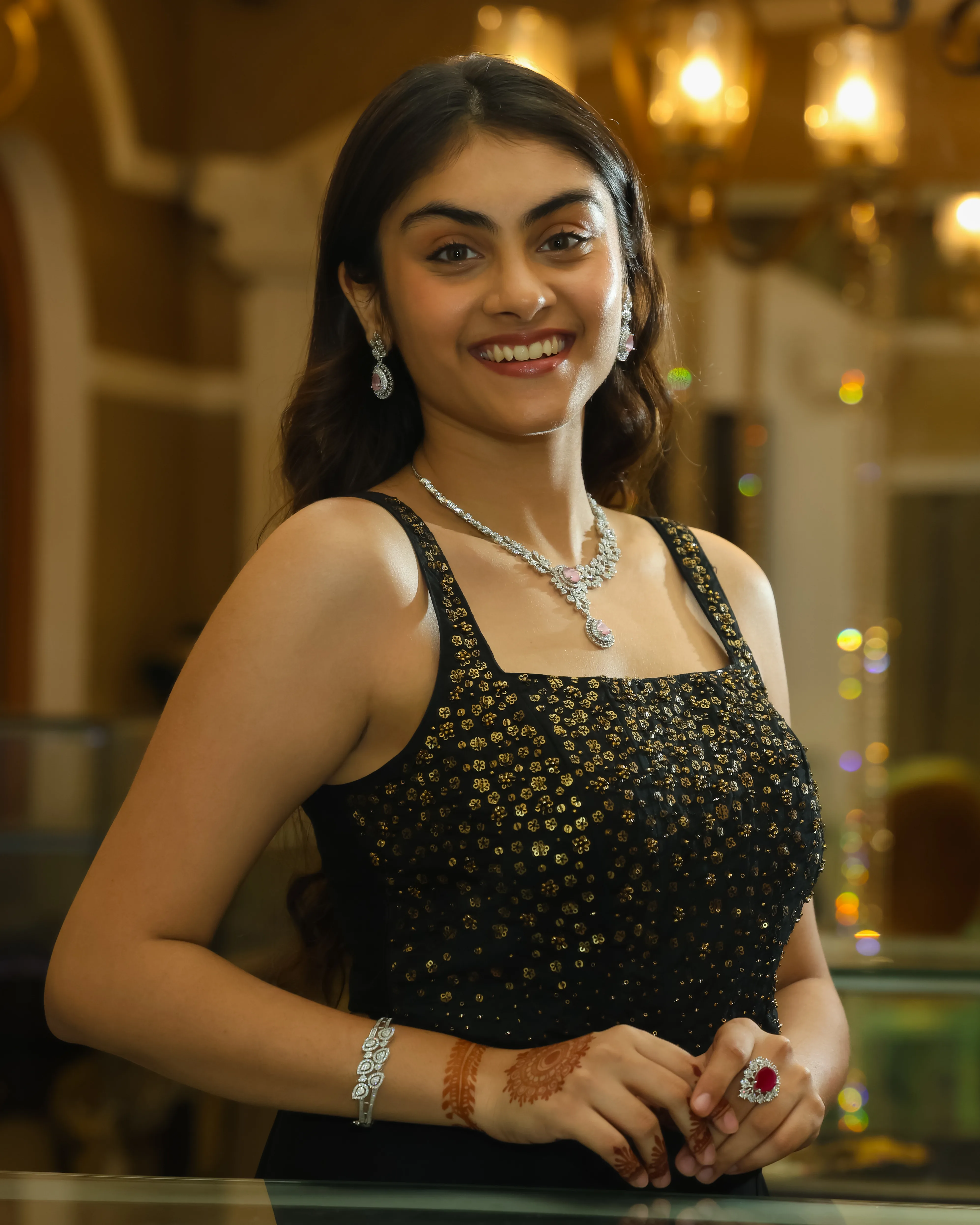 Smiling model in a black embellished top with a diamond-look necklace, bracelet and red stone cocktail ring